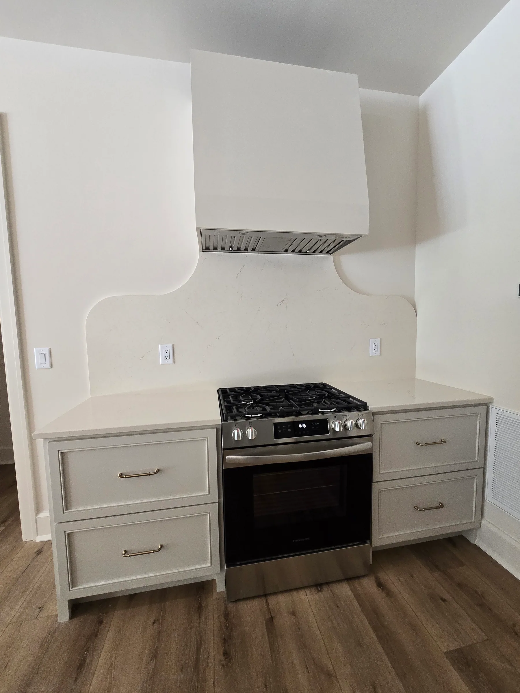 Painted base cabinets with drawers on both sides of a range, under a curved plaster range hood