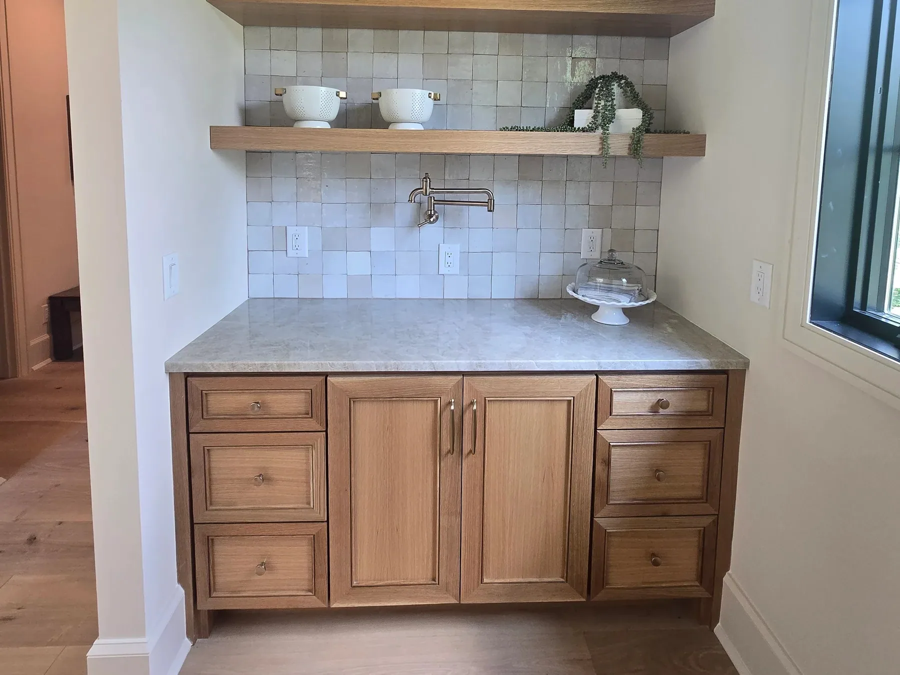 An oak beverage station with inset drawers and doors, a stone top, a pot filler and open oak shelves