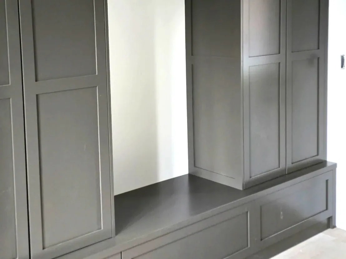 A built-in drop zone with tall dark painted shaker lockers on each side of a bench with drawers below